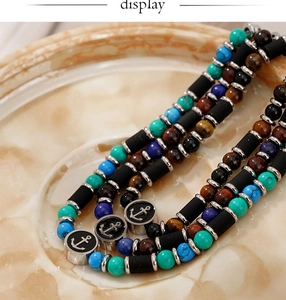 Gros plan du bracelet en perles avec oeil de tigre, turquoise et pendentif ancre sur marbre