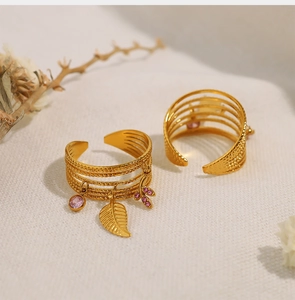 Detail of adjustable gold ring set with leaf charm and pink gemstone on beige fabric