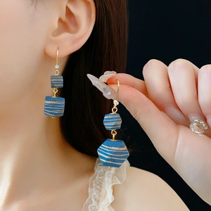 Blue geometric earrings with gold stripes worn by model against dark background