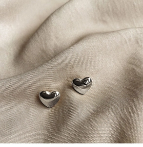 Macro shot of silver heart-shaped stud earrings on elegant champagne silk fabric
