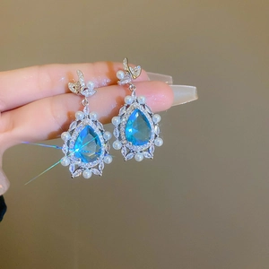 Detailed view of silver earrings with blue teardrop gems and white pearl accents