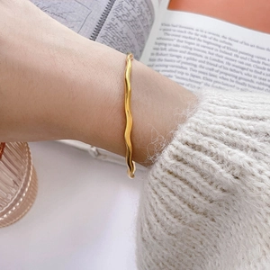 Detailed view of a golden wavy bangle bracelet worn over a beige knit sweater sleeve