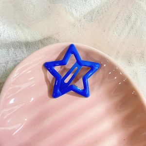 Close-up of a blue star-shaped hollow hair clip on a pink ceramic shell plate