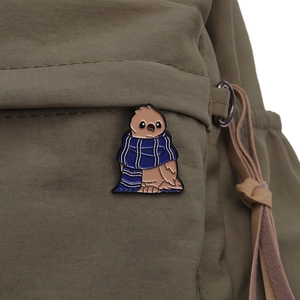 Gros plan d'un pin's chouette en émail avec écharpe sur la bandoulière d'un sac vert