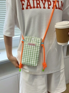 Green and white checkered canvas mini crossbody phone bag with orange rope strap shown on model