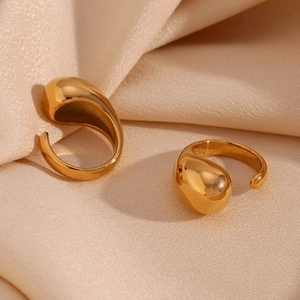 Detail of 18K gold-plated teardrop open rings on elegant beige silk fabric texture