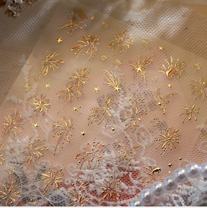 Detailed macro view of golden firework and butterfly nail stickers on lace background