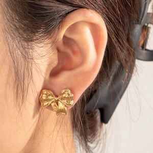 Elegant gold bow-shaped stud earrings in polished stainless steel worn by a model