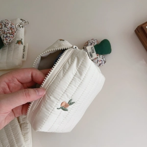 Detailed macro view of quilted cotton pouch featuring embroidered peach and woven label