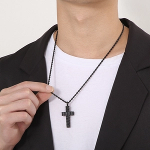 Detail of a black punk-style cross pendant with textured finish on a black rope chain