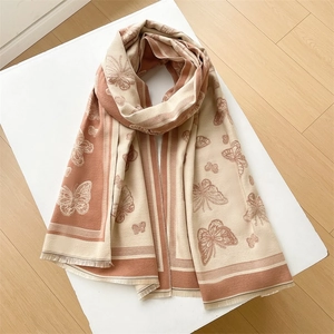 Flat lay detail of beige and terracotta butterfly scarf with tassels on wood background