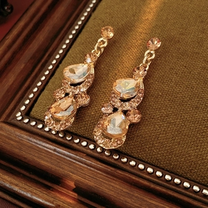 Détail de boucles d'oreilles vintage en or et cristaux champagne sur velours vert
