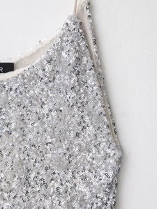 Détail macro de paillettes argentées sur maille beige avec fines bretelles souples