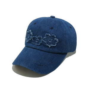 Detail of dark blue denim baseball cap featuring distressed floral embroidery patches