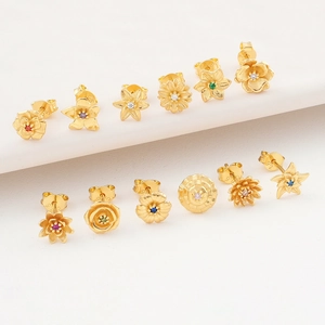 Macro view of assorted gold birth flower stud earrings with colorful gemstones on a white stand