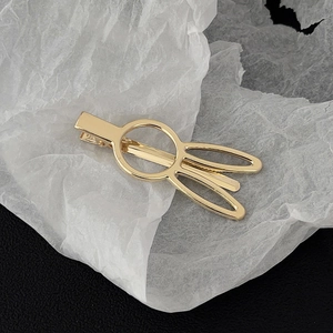 Macro shot of gold metal geometric rabbit ear hair clip on textured black background