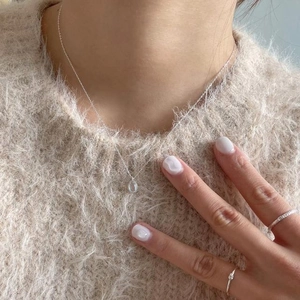 Detail of 925 sterling silver oval pendant necklace and rings on beige sweater