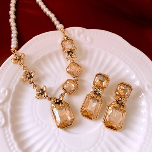 Detailed view of amber gemstone jewelry set with pearl chain on red velvet background