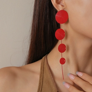 Detail of red tiered disc tassel earrings with textured metallic finish on model