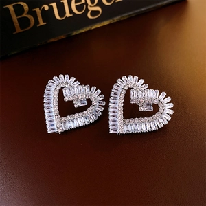 Detail shot of heart-shaped silver earrings with baguette zircon stones on leather