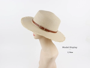 Detail of beige straw boater hat featuring frayed brim and leather belt with metal buckle