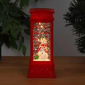 Close-up of a lit red telephone booth lantern with a snowman and swirling glitter snow