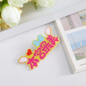 Close-up of a yellow acrylic brooch with cute wings and Chinese text on a white background