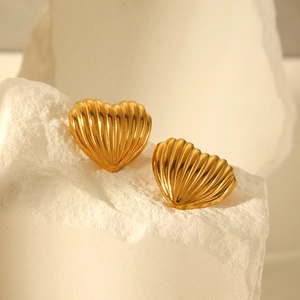 Macro detail of heart-shaped 18k gold earrings with linear texture on white stone base