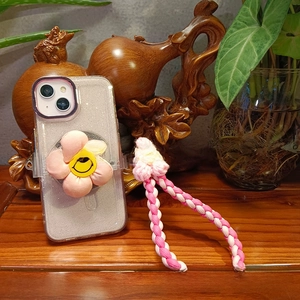 Detail of pink knitted flower phone case with matching braided wrist strap and smiley face