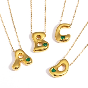 Detail of 18k gold plated bubble letter pendants with green heart-shaped gemstones