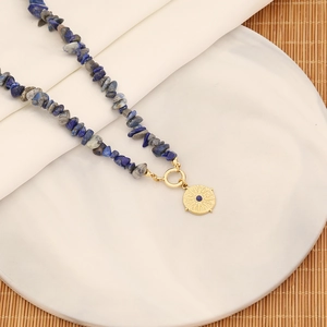 Dettaglio di collana di perline in pietra naturale con ciondolo a sole dorato su piatto