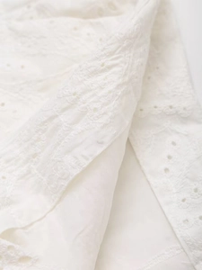 Close-up of white embroidered fabric featuring intricate hollow floral patterns and textures