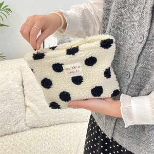 Close-up of fluffy white plush makeup bag with black polka dots held by a model