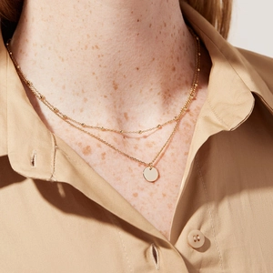 Close-up of double-layer 18K gold-plated necklace with beads and a round disc pendant