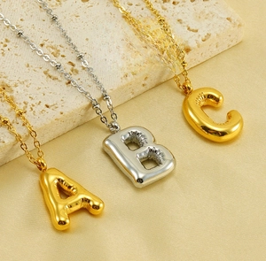 Detail of 18K gold and silver bubble letter necklaces A, B, C on silk background