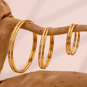 Three sizes of gold double hoop earrings displayed on a natural wood branch