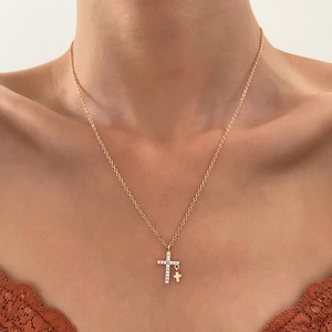 Detail van de gouden ketting met dubbele kruishanger en strassteentjes om de nek