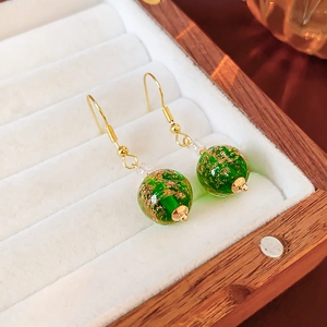 Macro detail of green glass earrings with gold foil inside on a white velvet jewelry box