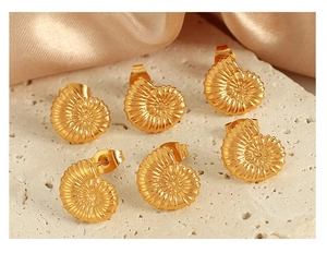 Detailed view of 18K gold plated conch spiral earrings on silk and stone background