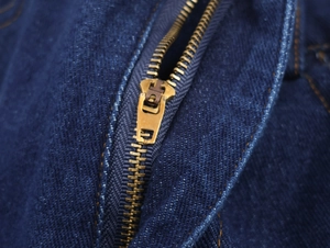 Détail de la fermeture éclair dorée et de la texture sur le jean et la chemise