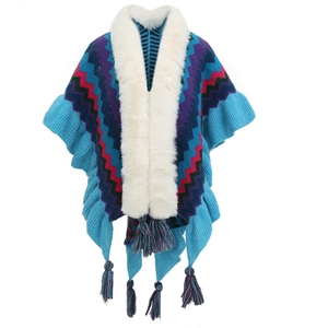 Detail of blue knit poncho featuring white fur collar and vibrant zigzag patterns with tassels