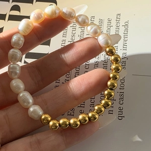 Detail of natural freshwater pearl and gold bead bracelet held by a hand on a magazine