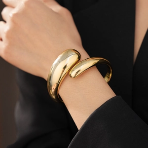 Close-up of a chunky gold pleated oval open bangle with a polished mirror finish on a model