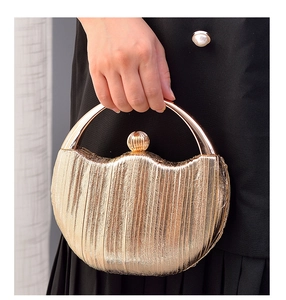 Golden clutch bag with pleated texture, circular metal handle, and spherical buckle detail