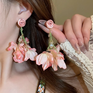 Pink fabric flower tassel earrings with green beads and gold chains on female model
