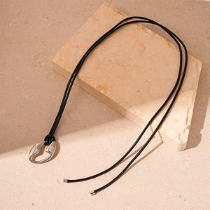 Minimalist silver irregular geometric pendant on black cord over neutral stone