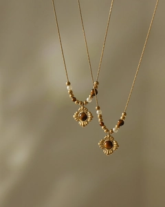 Detail of vintage gold flower pendants with tiger eye stone and white pearls on a soft background