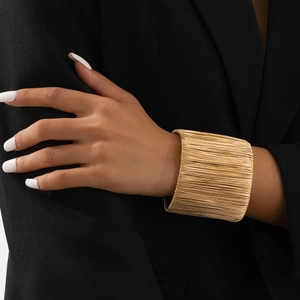 Close-up of a gold multi-layer woven wide bangle on a model wrist against black attire