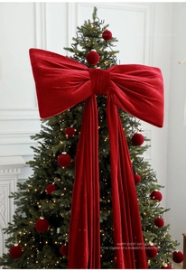Close-up of a giant burgundy velvet bow as a Christmas tree topper with matching red baubles