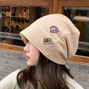 Beige knit bucket hat with creative enamel pins featuring book and flower designs